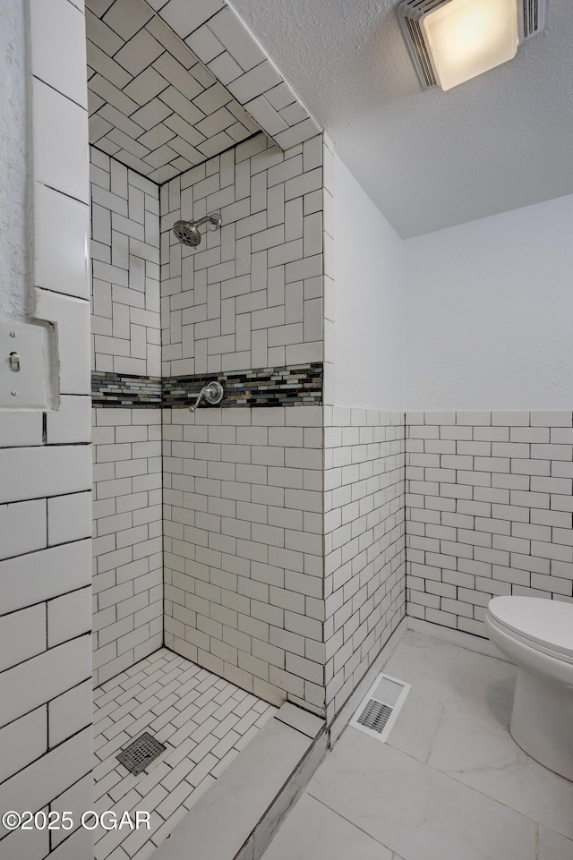 bathroom featuring toilet, a tile shower, tile walls, and a textured ceiling