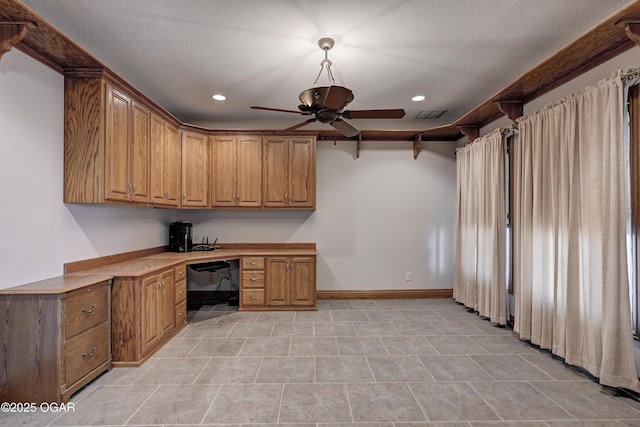 unfurnished office with ceiling fan, built in desk, and a textured ceiling