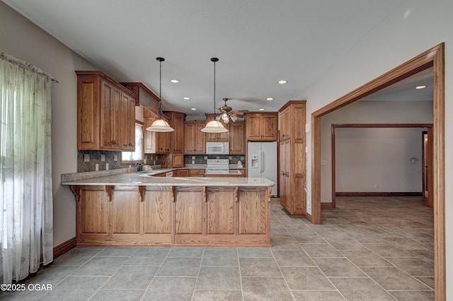 kitchen featuring a breakfast bar area, hanging light fixtures, kitchen peninsula, white appliances, and backsplash