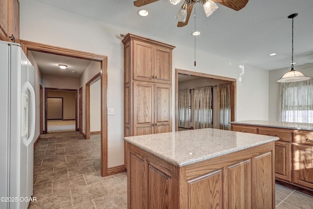 kitchen with ceiling fan, hanging light fixtures, a center island, light stone counters, and white fridge with ice dispenser