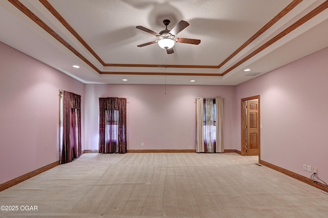 empty room featuring ceiling fan, light colored carpet, ornamental molding, and a raised ceiling