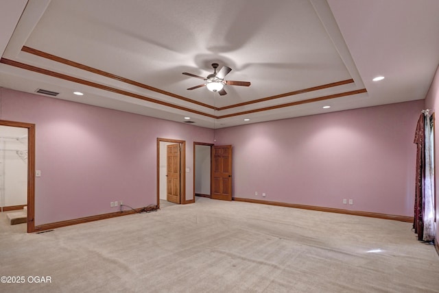 empty room with crown molding, ceiling fan, a tray ceiling, and light carpet