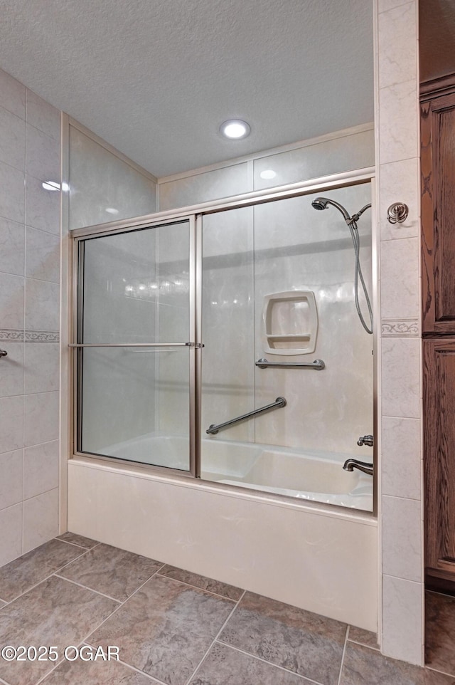 bathroom with shower / bath combination with glass door, a textured ceiling, and tile walls