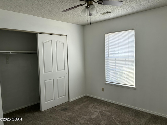 unfurnished bedroom featuring ceiling fan, a closet, a textured ceiling, and dark colored carpet