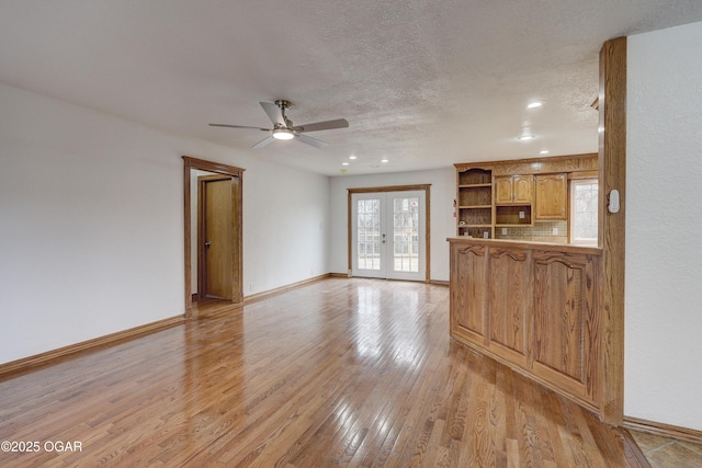 unfurnished living room with a textured ceiling, french doors, a healthy amount of sunlight, and light wood-type flooring