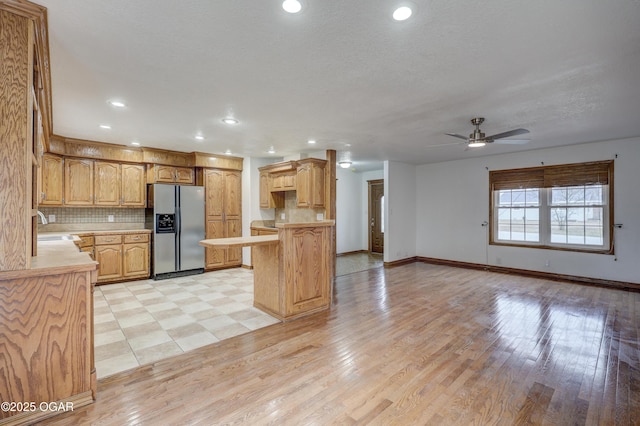 kitchen with sink, kitchen peninsula, decorative backsplash, and stainless steel fridge with ice dispenser