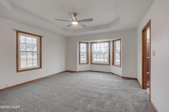 unfurnished room featuring ceiling fan, a tray ceiling, a healthy amount of sunlight, and carpet flooring