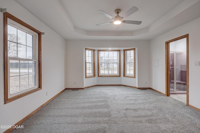 carpeted empty room featuring ceiling fan, a tray ceiling, and a wealth of natural light