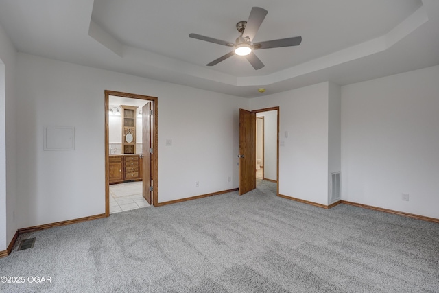 empty room featuring light colored carpet, a raised ceiling, and ceiling fan