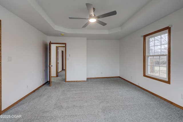 empty room featuring light carpet, a tray ceiling, and ceiling fan