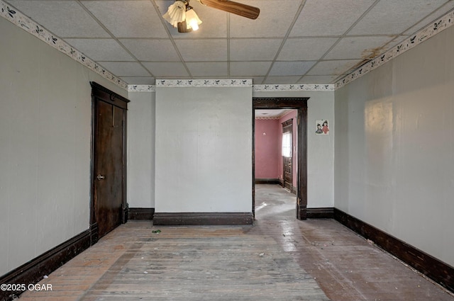 empty room with ceiling fan, wood-type flooring, and a drop ceiling