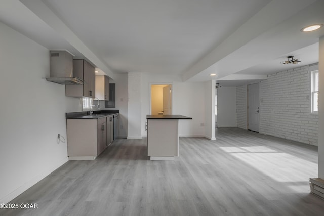 kitchen with wall chimney exhaust hood, sink, kitchen peninsula, brick wall, and light hardwood / wood-style floors