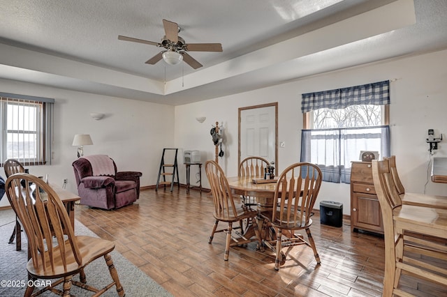 dining area with wood-type flooring, ceiling fan, a textured ceiling, and a tray ceiling