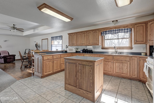 kitchen with sink, white appliances, light tile patterned floors, a tray ceiling, and a kitchen island