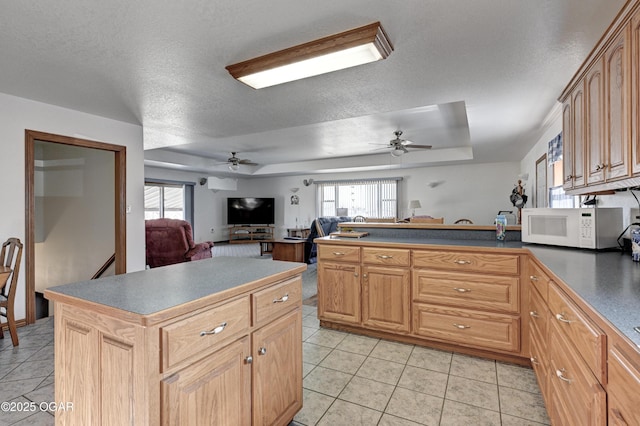 kitchen with a raised ceiling, a kitchen island, light tile patterned floors, and a textured ceiling