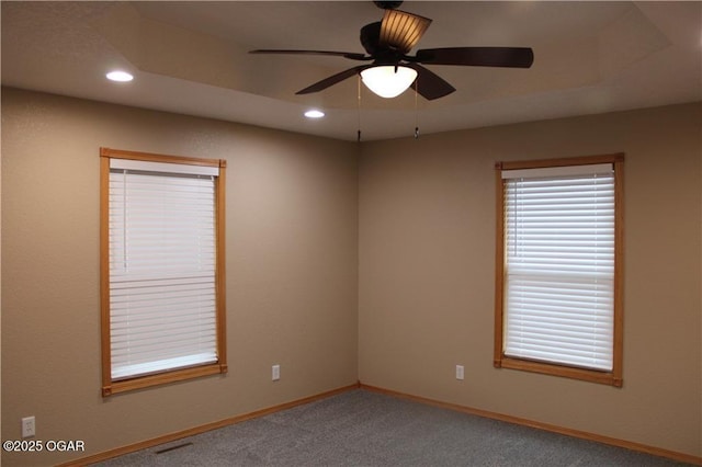 carpeted spare room featuring a raised ceiling and ceiling fan