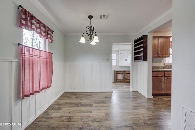 unfurnished dining area with a wainscoted wall, dark wood-style flooring, visible vents, and a notable chandelier