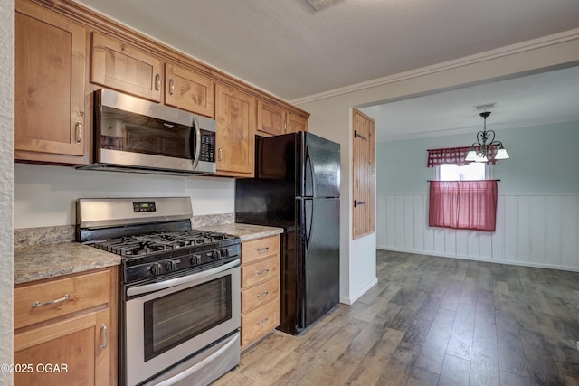 kitchen featuring a wainscoted wall, appliances with stainless steel finishes, brown cabinetry, and light wood-style floors