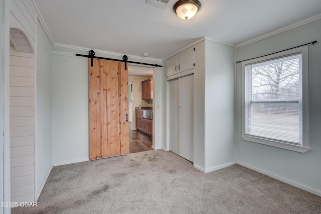 unfurnished bedroom featuring carpet floors, a closet, a barn door, ornamental molding, and baseboards