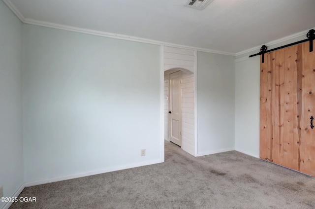 carpeted empty room with baseboards, a barn door, visible vents, and crown molding