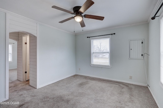 carpeted spare room with ornamental molding, arched walkways, baseboards, and a ceiling fan