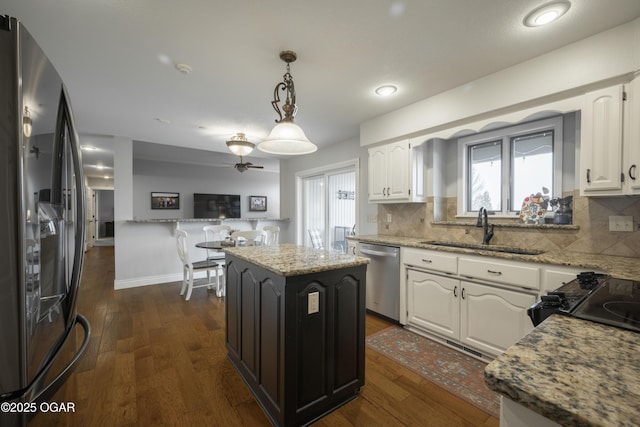 kitchen with sink, light stone counters, appliances with stainless steel finishes, a kitchen island, and white cabinets