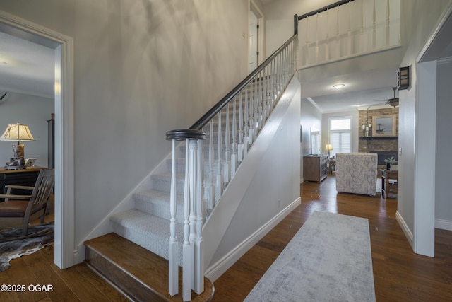 stairway with wood-type flooring, a towering ceiling, ceiling fan, and a fireplace