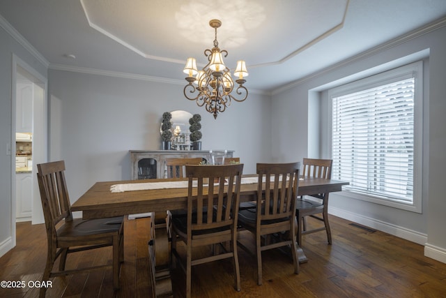 dining room with dark wood-type flooring, a tray ceiling, and crown molding