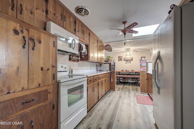 kitchen featuring white appliances, a skylight, light hardwood / wood-style flooring, ceiling fan, and decorative backsplash