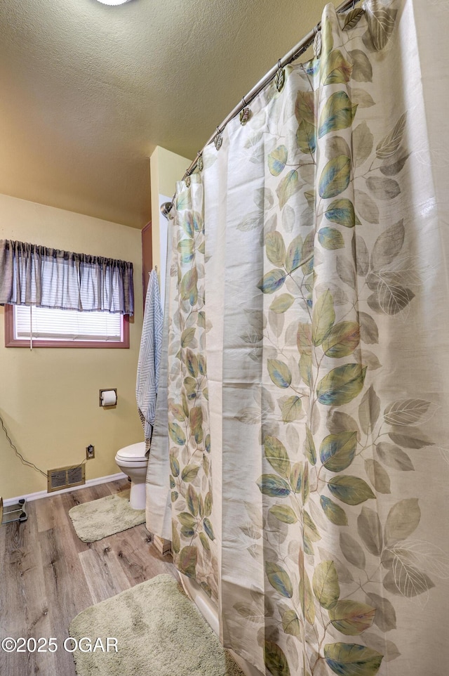 bathroom with a shower with curtain, toilet, hardwood / wood-style floors, and a textured ceiling