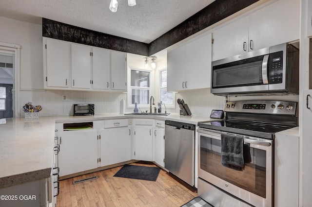 kitchen with sink, white cabinetry, light hardwood / wood-style flooring, a textured ceiling, and appliances with stainless steel finishes