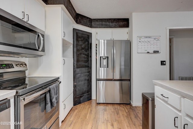 kitchen with appliances with stainless steel finishes, a textured ceiling, white cabinets, and light hardwood / wood-style floors