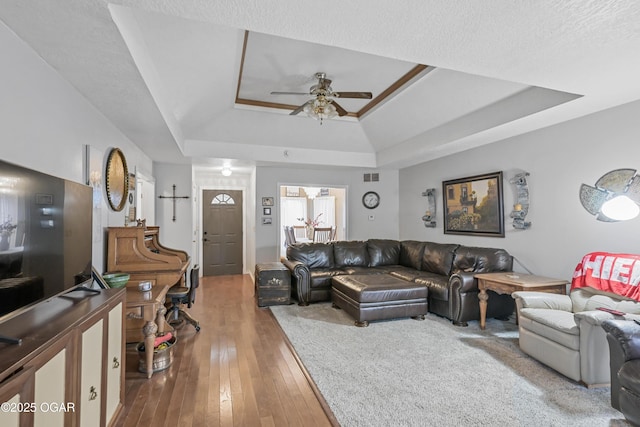 living room with a tray ceiling, wood-type flooring, and ceiling fan