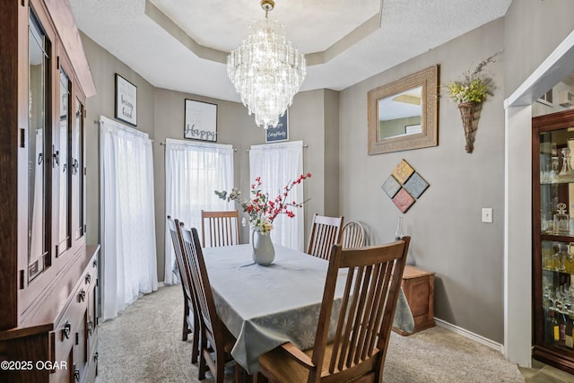 dining room with a chandelier, a raised ceiling, light carpet, and a textured ceiling