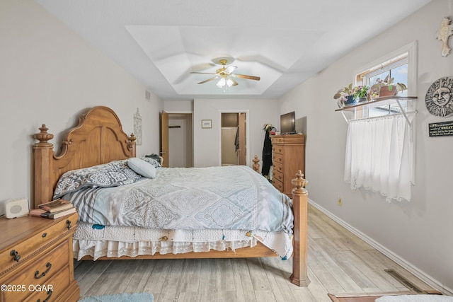 bedroom featuring a raised ceiling, ceiling fan, and light wood-type flooring