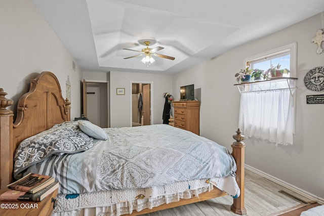 bedroom with ceiling fan, a tray ceiling, and light hardwood / wood-style floors