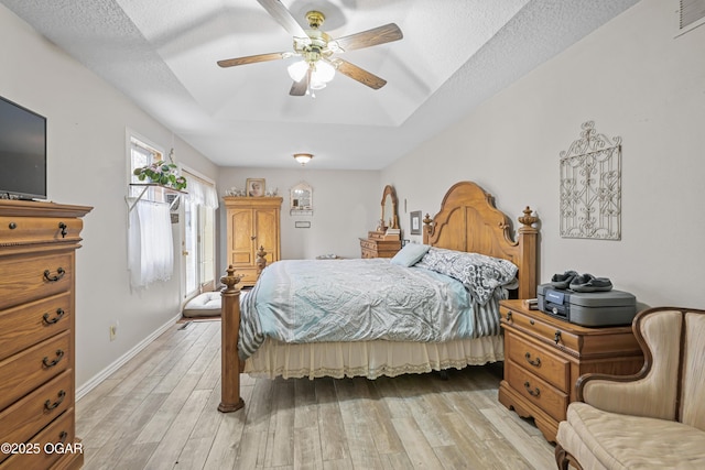 bedroom with light wood-type flooring, access to exterior, ceiling fan, a raised ceiling, and a textured ceiling