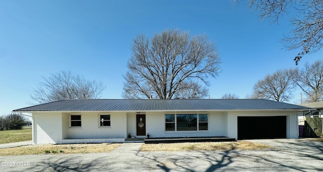 ranch-style home featuring aphalt driveway, an attached garage, brick siding, and metal roof