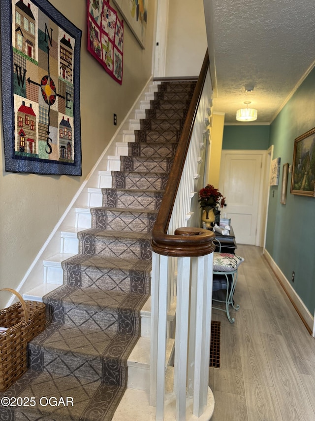 staircase with ornamental molding, wood-type flooring, and a textured ceiling