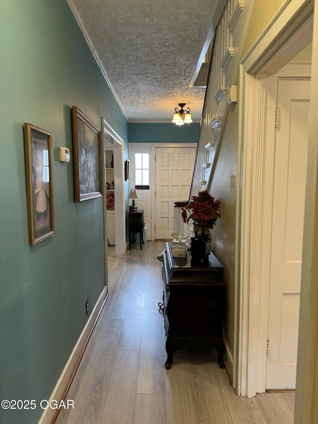 corridor featuring ornamental molding, a textured ceiling, and light hardwood / wood-style floors