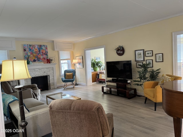 living room featuring ornamental molding, a stone fireplace, and light hardwood / wood-style flooring