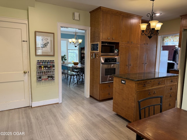 kitchen featuring built in microwave, light hardwood / wood-style flooring, dark stone countertops, pendant lighting, and oven