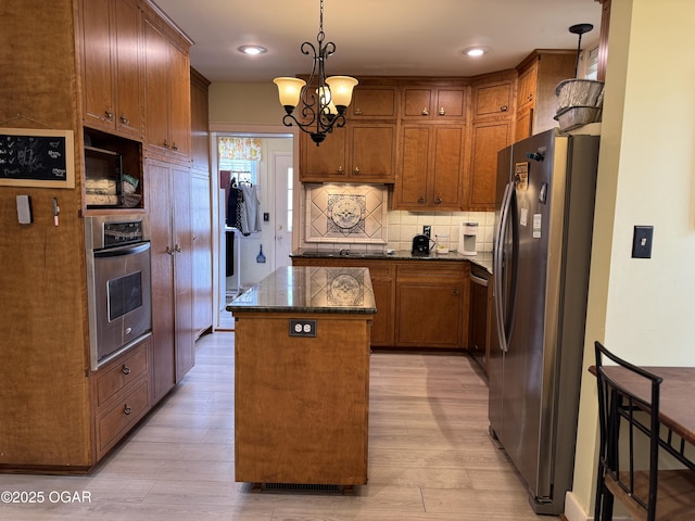 kitchen featuring hanging light fixtures, light wood-type flooring, appliances with stainless steel finishes, a kitchen island, and decorative backsplash