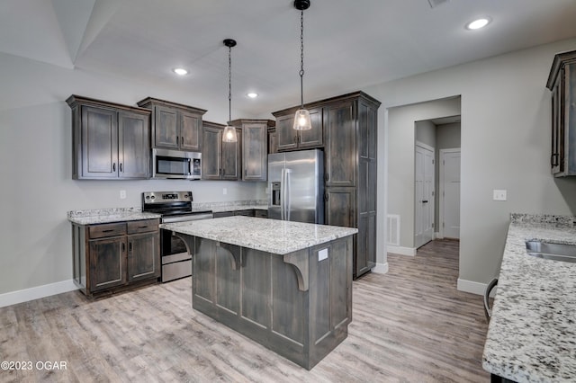 kitchen with a kitchen breakfast bar, hanging light fixtures, stainless steel appliances, light stone countertops, and light hardwood / wood-style flooring