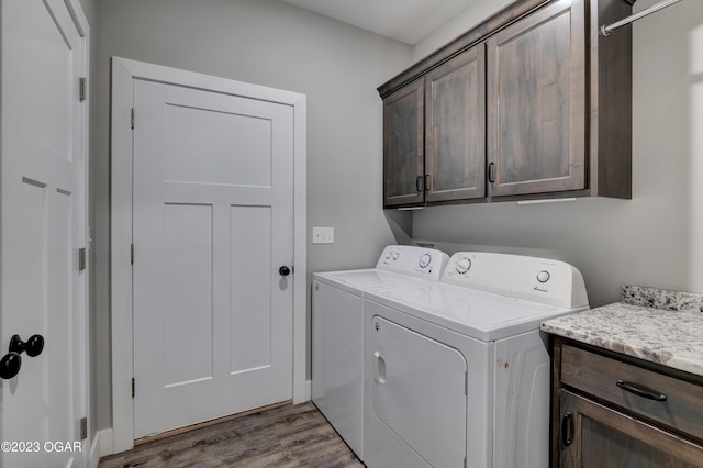 clothes washing area featuring separate washer and dryer, wood-type flooring, and cabinets