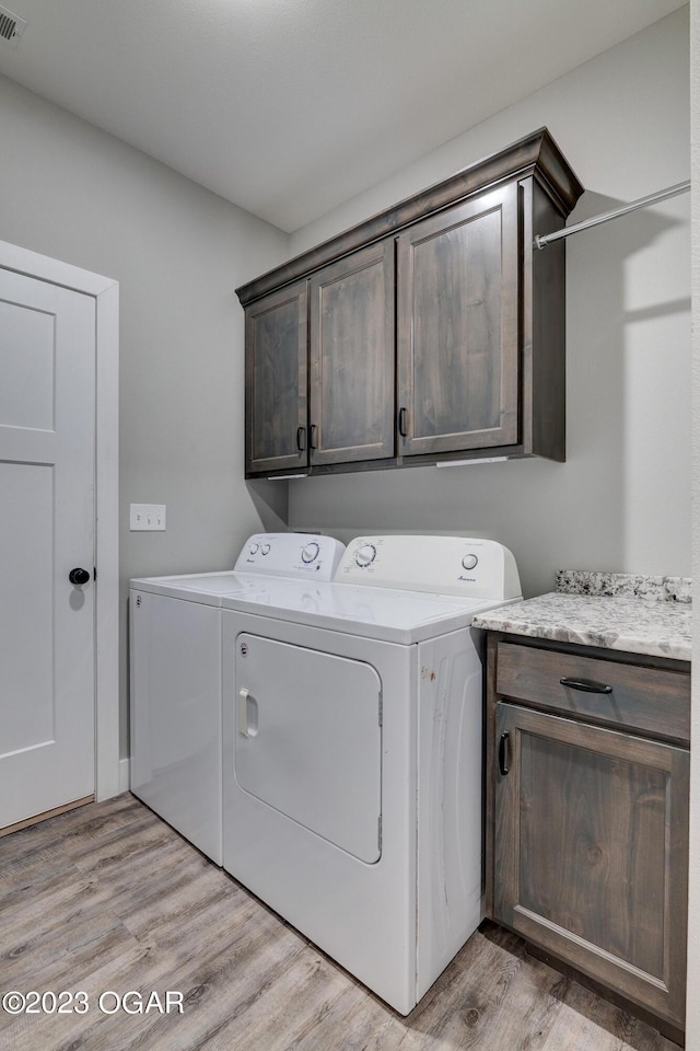 laundry area featuring cabinets, washing machine and clothes dryer, and light hardwood / wood-style flooring