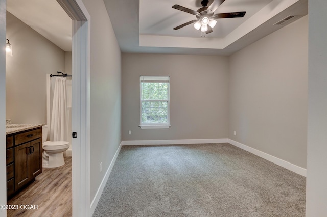 carpeted spare room featuring a tray ceiling and ceiling fan