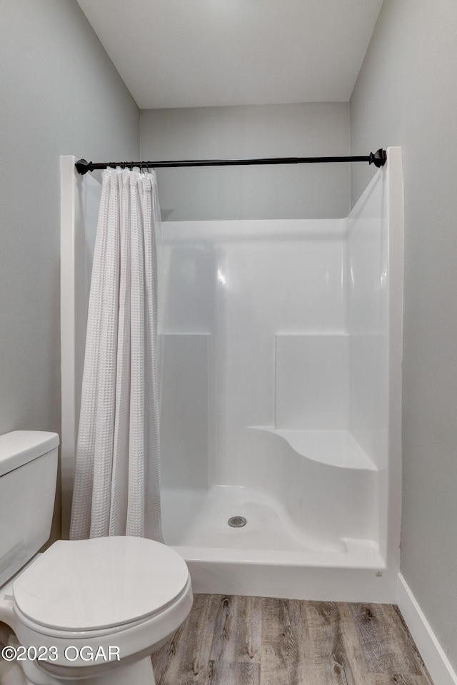 bathroom with walk in shower, toilet, and hardwood / wood-style floors