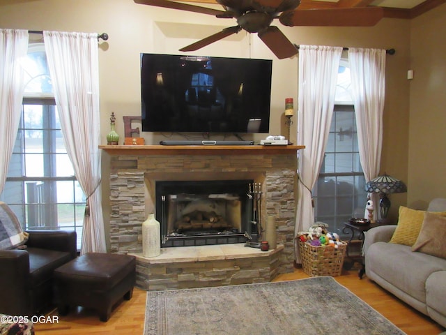 living room featuring hardwood / wood-style flooring, a stone fireplace, a healthy amount of sunlight, and ceiling fan