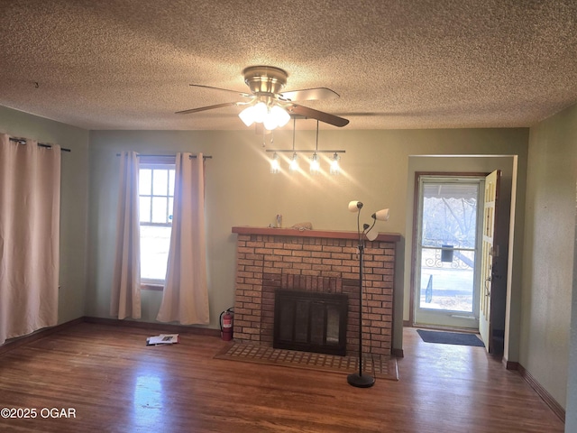 unfurnished living room with wood-type flooring, a brick fireplace, a textured ceiling, and ceiling fan